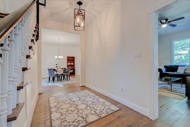 foyer entrance featuring wood-type flooring, a ceiling fan, a chandelier, and baseboards