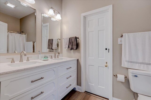 bathroom featuring double vanity, wood finished floors, baseboards, and toilet