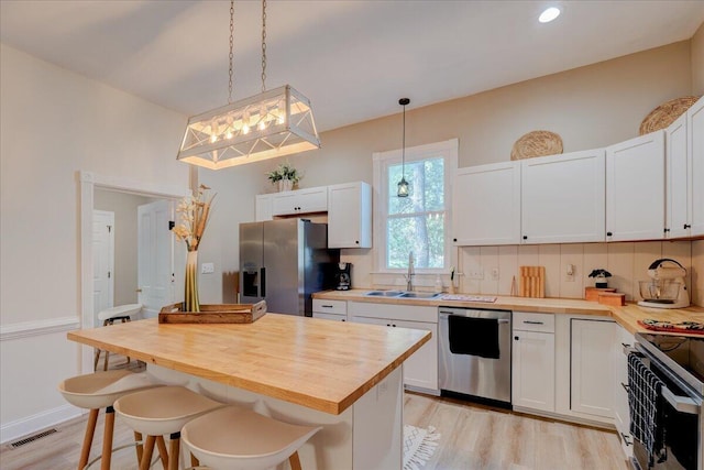 kitchen featuring stainless steel appliances, butcher block counters, a sink, light wood-type flooring, and recessed lighting
