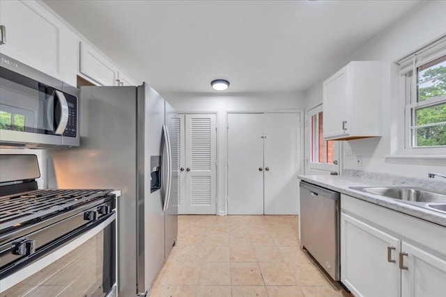 kitchen featuring stainless steel appliances, white cabinets, light countertops, a sink, and light tile patterned floors