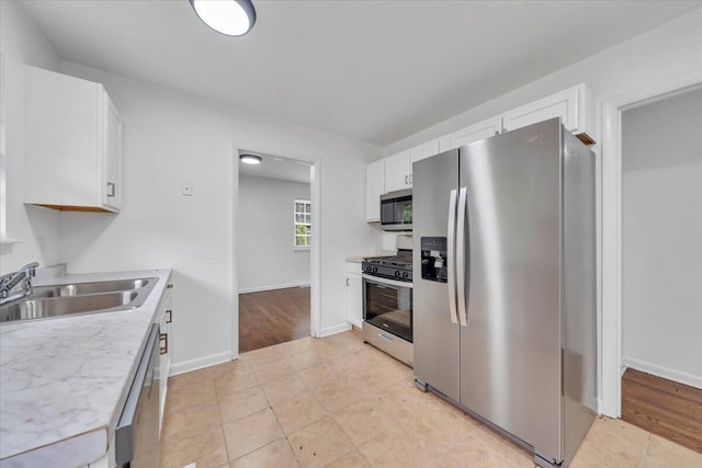 kitchen featuring stainless steel appliances, a sink, white cabinets, light countertops, and baseboards