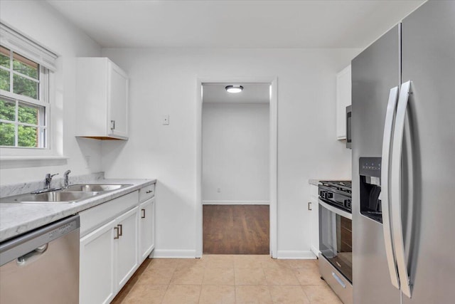 kitchen featuring appliances with stainless steel finishes, a sink, white cabinetry, light countertops, and baseboards