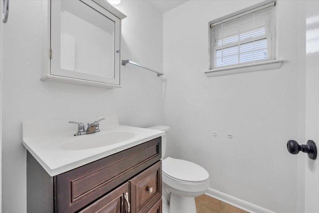 half bathroom with vanity, toilet, baseboards, and tile patterned flooring