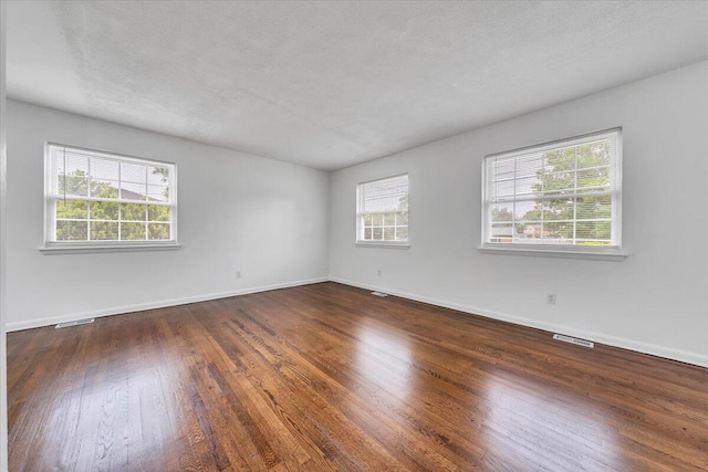 unfurnished room with healthy amount of natural light, wood finished floors, and baseboards