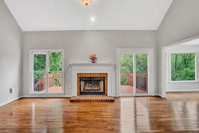 unfurnished living room with wood-type flooring, lofted ceiling, a brick fireplace, and baseboards