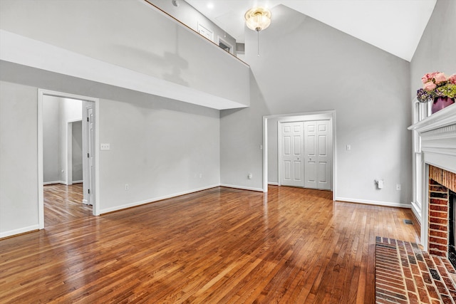unfurnished living room featuring a towering ceiling, a fireplace, wood-type flooring, and baseboards