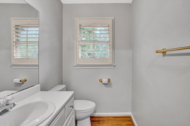 half bath featuring toilet, wood finished floors, baseboards, and vanity