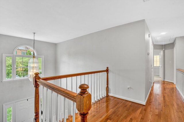 hallway featuring attic access, hardwood / wood-style flooring, an upstairs landing, and baseboards