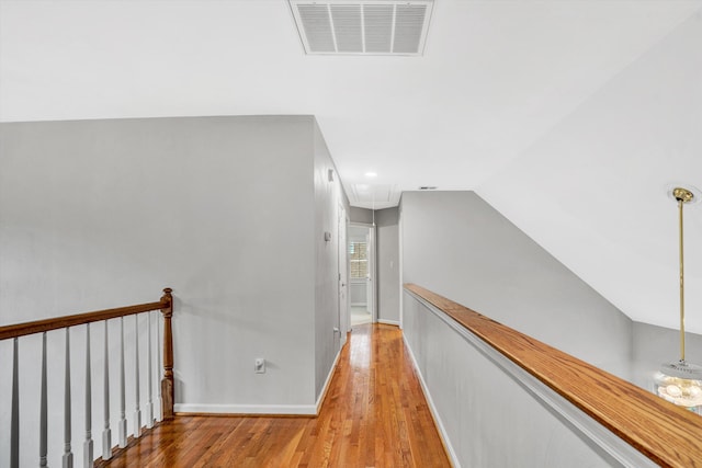 corridor featuring attic access, wood finished floors, baseboards, an upstairs landing, and vaulted ceiling