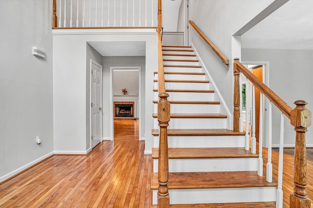 staircase with hardwood / wood-style floors, baseboards, and a fireplace