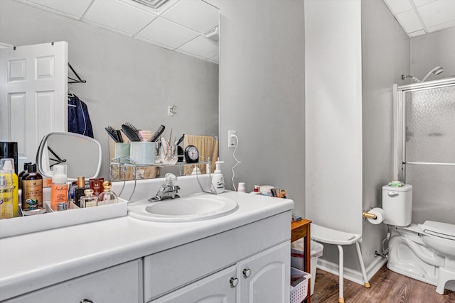 bathroom with a paneled ceiling, wood finished floors, vanity, a shower with door, and toilet