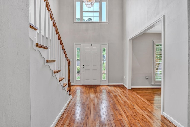 foyer featuring wood-type flooring, a high ceiling, baseboards, stairway, and a chandelier