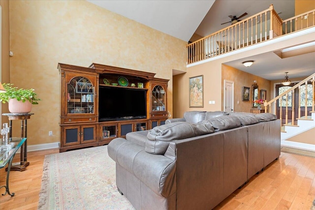 living room featuring high vaulted ceiling, stairway, light wood-type flooring, baseboards, and a ceiling fan