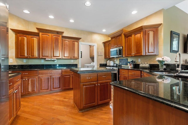 kitchen featuring appliances with stainless steel finishes, a sink, light wood-style floors, recessed lighting, and dark stone counters