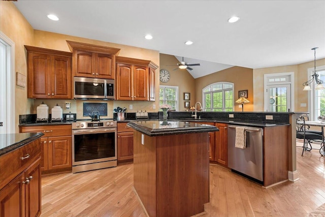 kitchen featuring stainless steel appliances, a center island, light wood-style floors, a sink, and a ceiling fan
