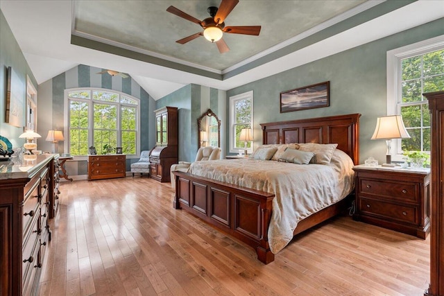 bedroom featuring light wood finished floors, a tray ceiling, baseboards, ornamental molding, and ceiling fan