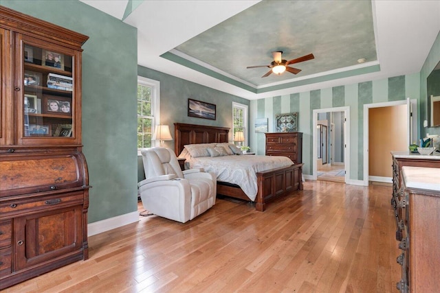 bedroom with a tray ceiling, light wood-style floors, baseboards, and a ceiling fan