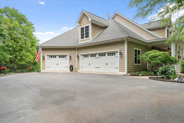 view of side of property featuring roof with shingles, an attached garage, fence, and asphalt driveway