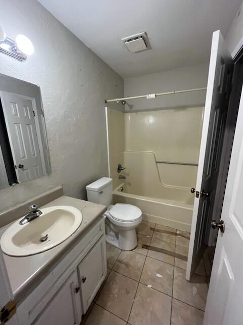 bathroom with vanity, toilet, a textured wall, shower / bathtub combination, and tile patterned floors