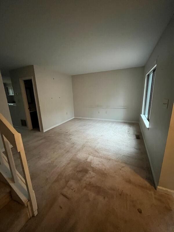 carpeted empty room with stairway and baseboards