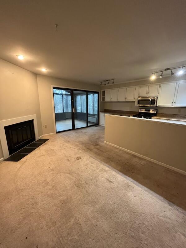 unfurnished living room featuring track lighting, light colored carpet, a glass covered fireplace, and baseboards