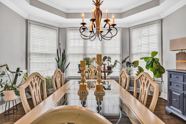 dining area with a chandelier, dark wood finished floors, plenty of natural light, ornamental molding, and a tray ceiling