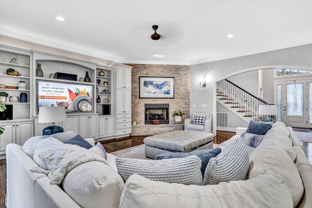 living area with stairway, dark wood finished floors, arched walkways, crown molding, and a stone fireplace