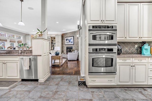 kitchen featuring stainless steel appliances, ornamental molding, light stone countertops, a large fireplace, and decorative backsplash