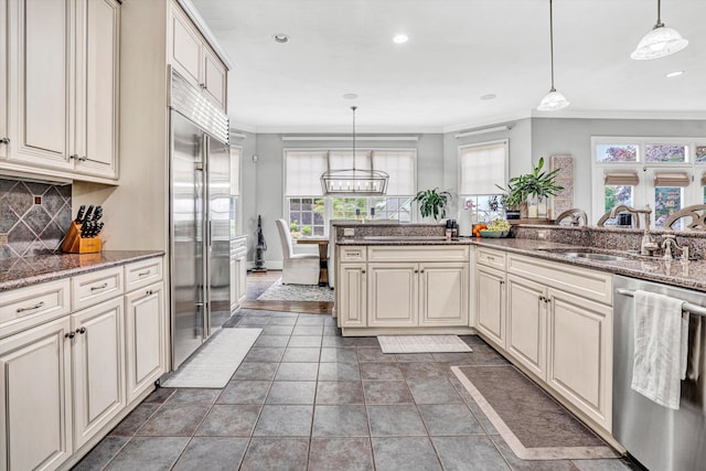 kitchen featuring stainless steel appliances, a sink, crown molding, cream cabinets, and decorative backsplash