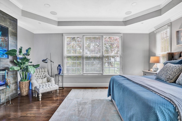 bedroom featuring a tray ceiling, wood finished floors, multiple windows, and ornamental molding
