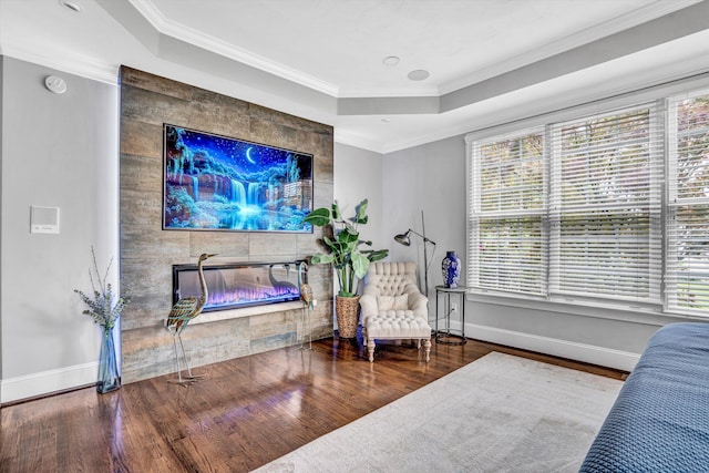 sitting room with a tile fireplace, wood finished floors, baseboards, a raised ceiling, and crown molding