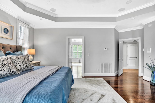 bedroom with a tray ceiling, wood finished floors, crown molding, and baseboards
