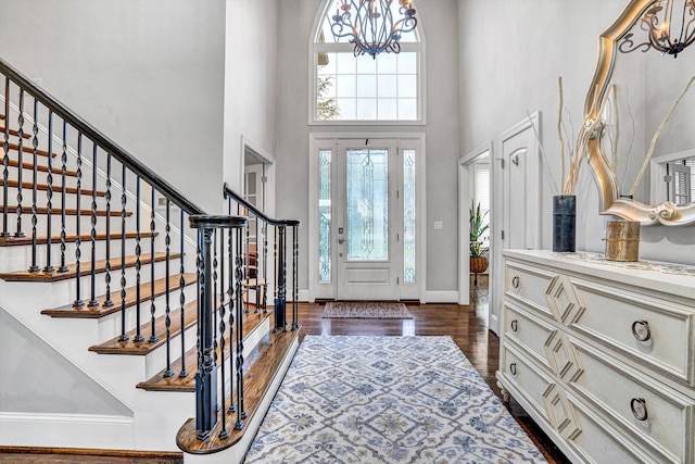 entrance foyer featuring a towering ceiling, dark wood finished floors, stairway, a chandelier, and baseboards