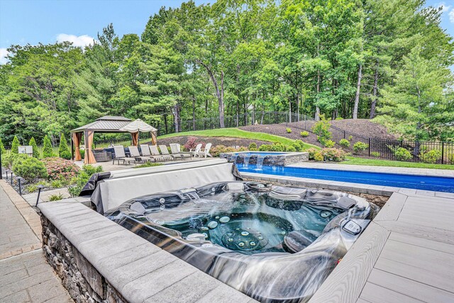 view of pool with a gazebo, a covered hot tub, a fenced backyard, and view of scattered trees
