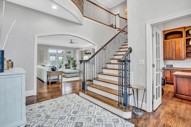 foyer entrance featuring arched walkways, french doors, wood finished floors, crown molding, and stairway