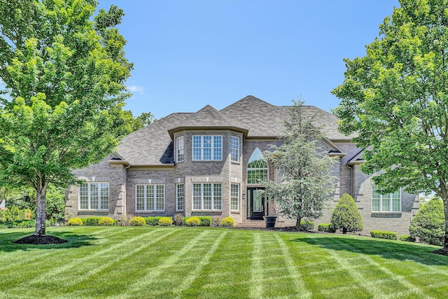 french provincial home with a front lawn and brick siding