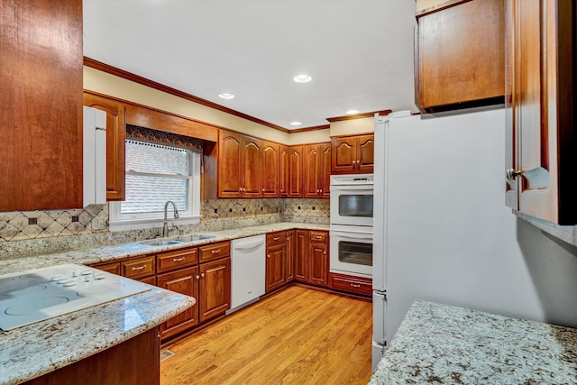 kitchen with white appliances, a sink, ornamental molding, light wood finished floors, and tasteful backsplash