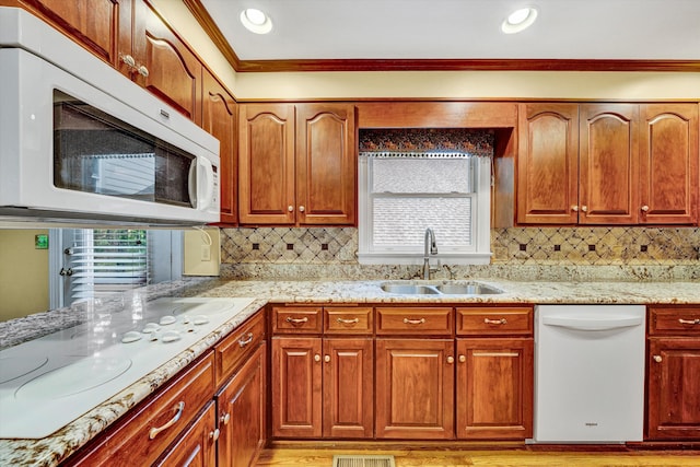 kitchen with white appliances, a sink, crown molding, light stone counters, and plenty of natural light