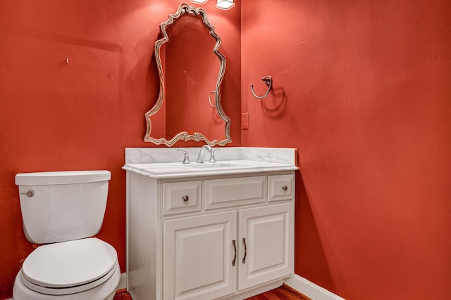 half bathroom featuring toilet, vanity, and baseboards