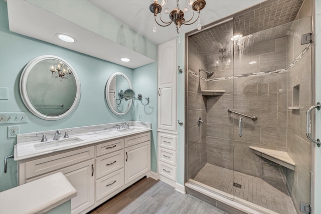 full bath featuring a chandelier, a shower stall, double vanity, and wood finished floors