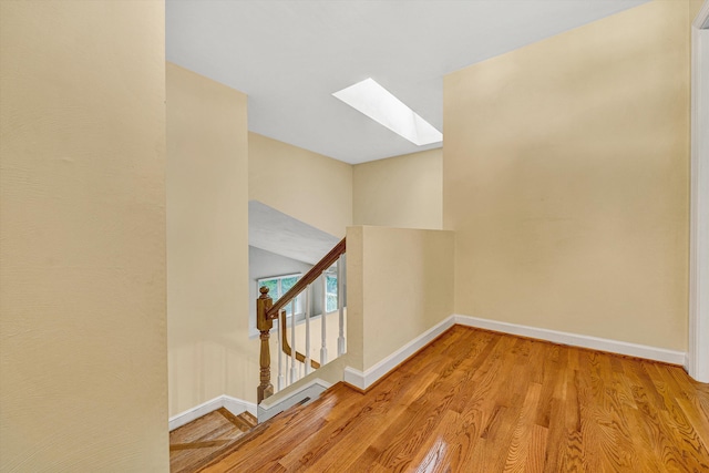 hallway featuring a skylight, wood finished floors, baseboards, and stairs