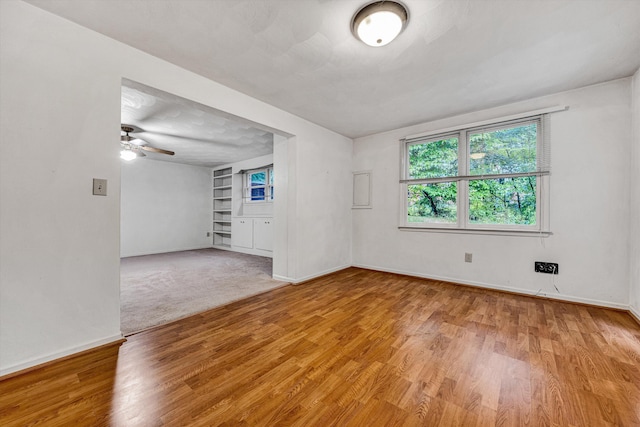 empty room featuring baseboards, light wood-style flooring, ceiling fan, and built in features