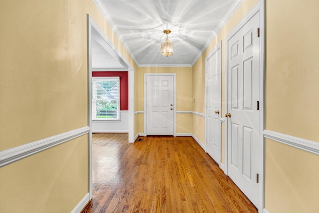 foyer entrance with crown molding, wood finished floors, baseboards, and a chandelier