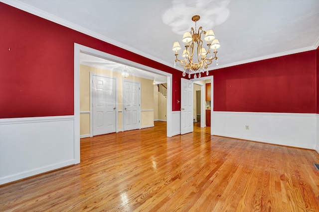 spare room with a chandelier, wood finished floors, crown molding, wainscoting, and baseboards