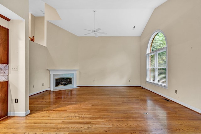 unfurnished living room with ceiling fan, high vaulted ceiling, light wood-type flooring, a premium fireplace, and baseboards
