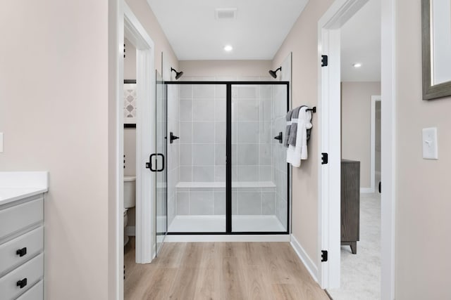 bathroom with a shower stall, toilet, wood finished floors, baseboards, and vanity