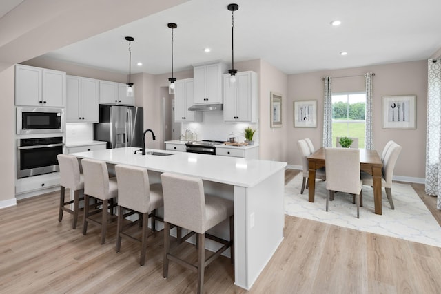 kitchen featuring appliances with stainless steel finishes, a sink, under cabinet range hood, a kitchen bar, and light wood-type flooring