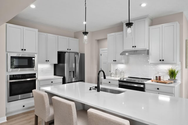 kitchen featuring stainless steel appliances, a sink, under cabinet range hood, tasteful backsplash, and light countertops