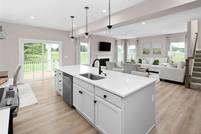 kitchen featuring a sink, stainless steel dishwasher, a fireplace, light wood-type flooring, and recessed lighting