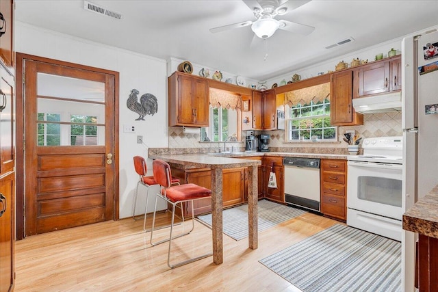kitchen with white appliances, under cabinet range hood, light wood finished floors, tasteful backsplash, and brown cabinets